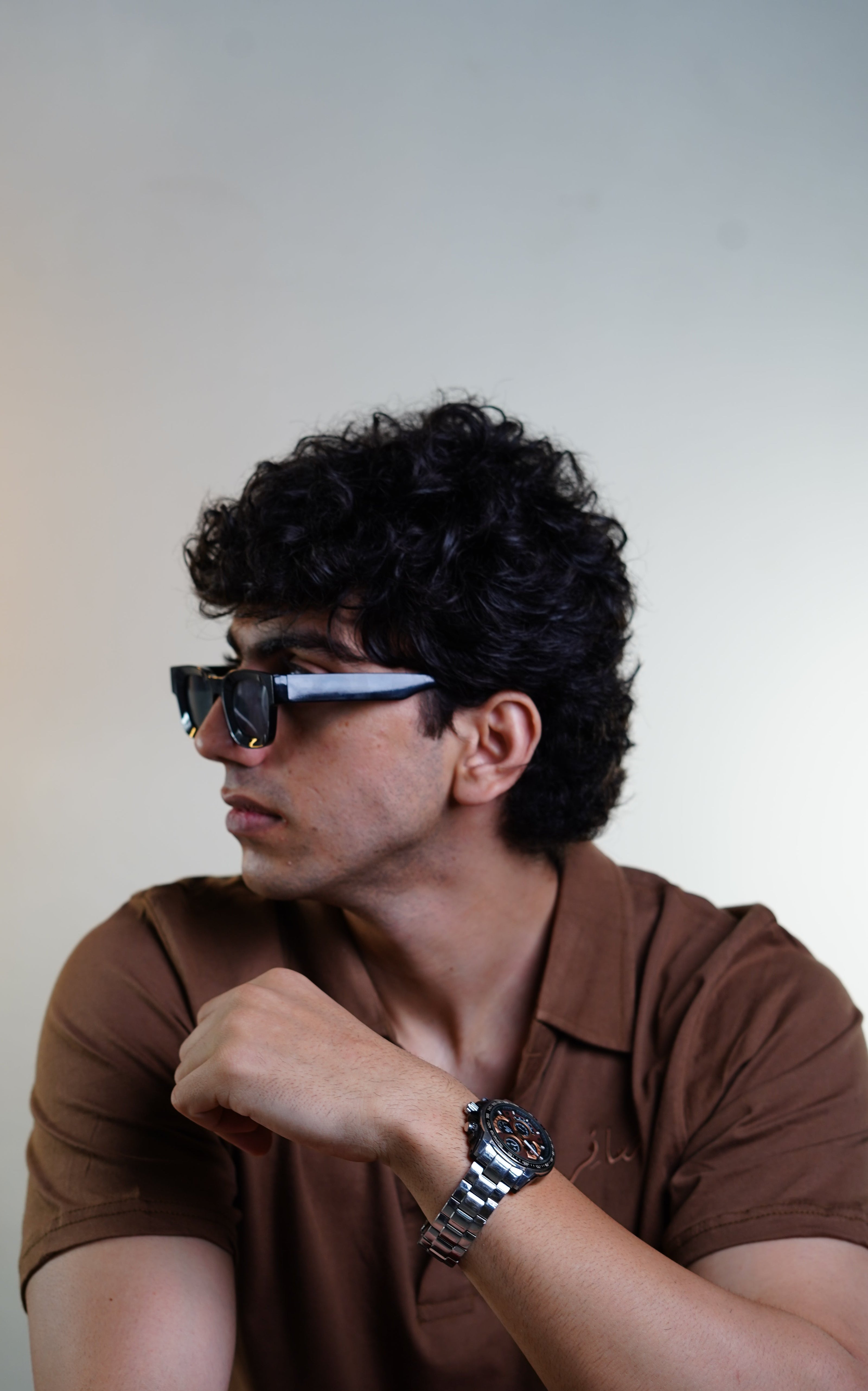 Man wearing sunglasses and a brown shirt against a plain background